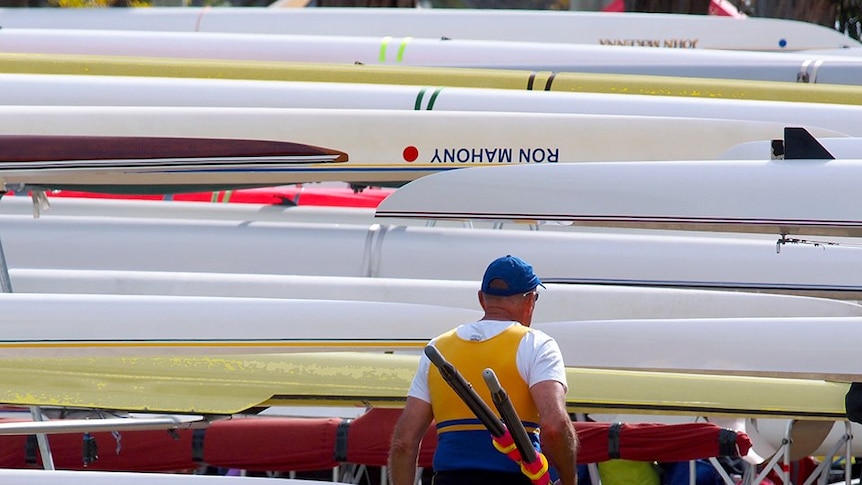 An elderly  rower carries his oars alongside boats