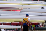 An elderly  rower carries his oars alongside boats