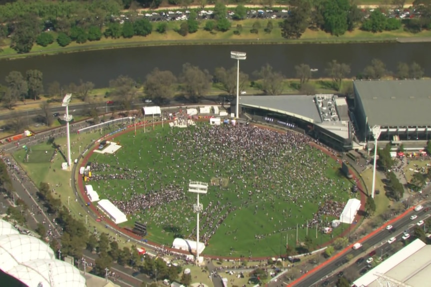 An aerial shot of a football field with people looking like tiny dots spread across the ground with a river flowing behind.