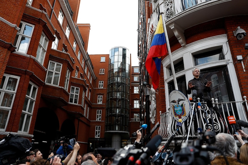 Un hombre hablando desde un balcón, con un gran contingente de medios debajo.