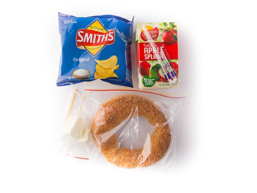 A sesame seed bagel and cream cheese, plain potato chips and an apple flavoured fruit box on a white background.