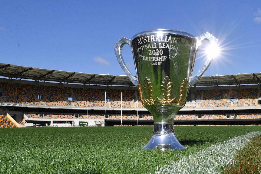 The AFL premiership cup glistens in the sunlight while sitting on the turf at the Gabba