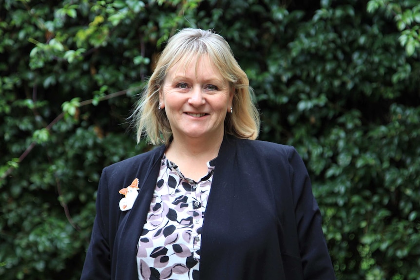 A woman standing in front of a hedge smiling and wearing a dog brooch