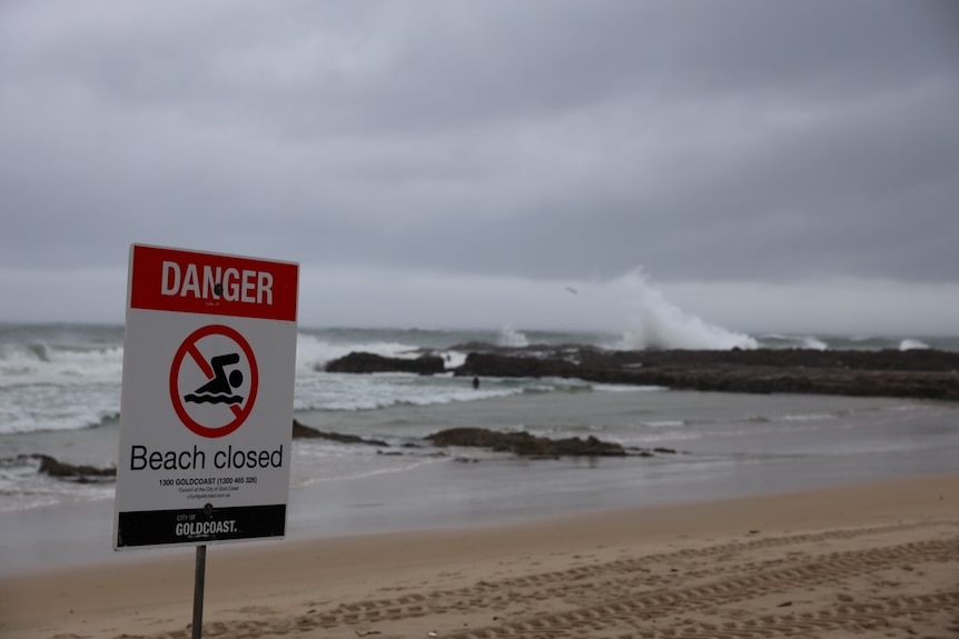 Beach closed sign on beach at Snapper Rocks with waves breaking over rocks in the background