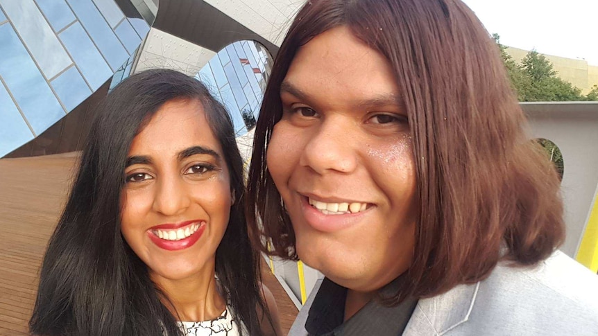 A young woman and a young man pose for a selfie at an event.
