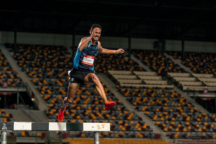 Matthew Clarke jumps over a steeple in a race with an empty stand in the background.