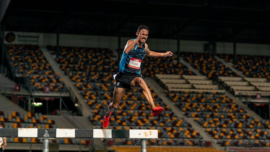 Matthew Clarke jumps over a steeple in a race with an empty stand in the background.