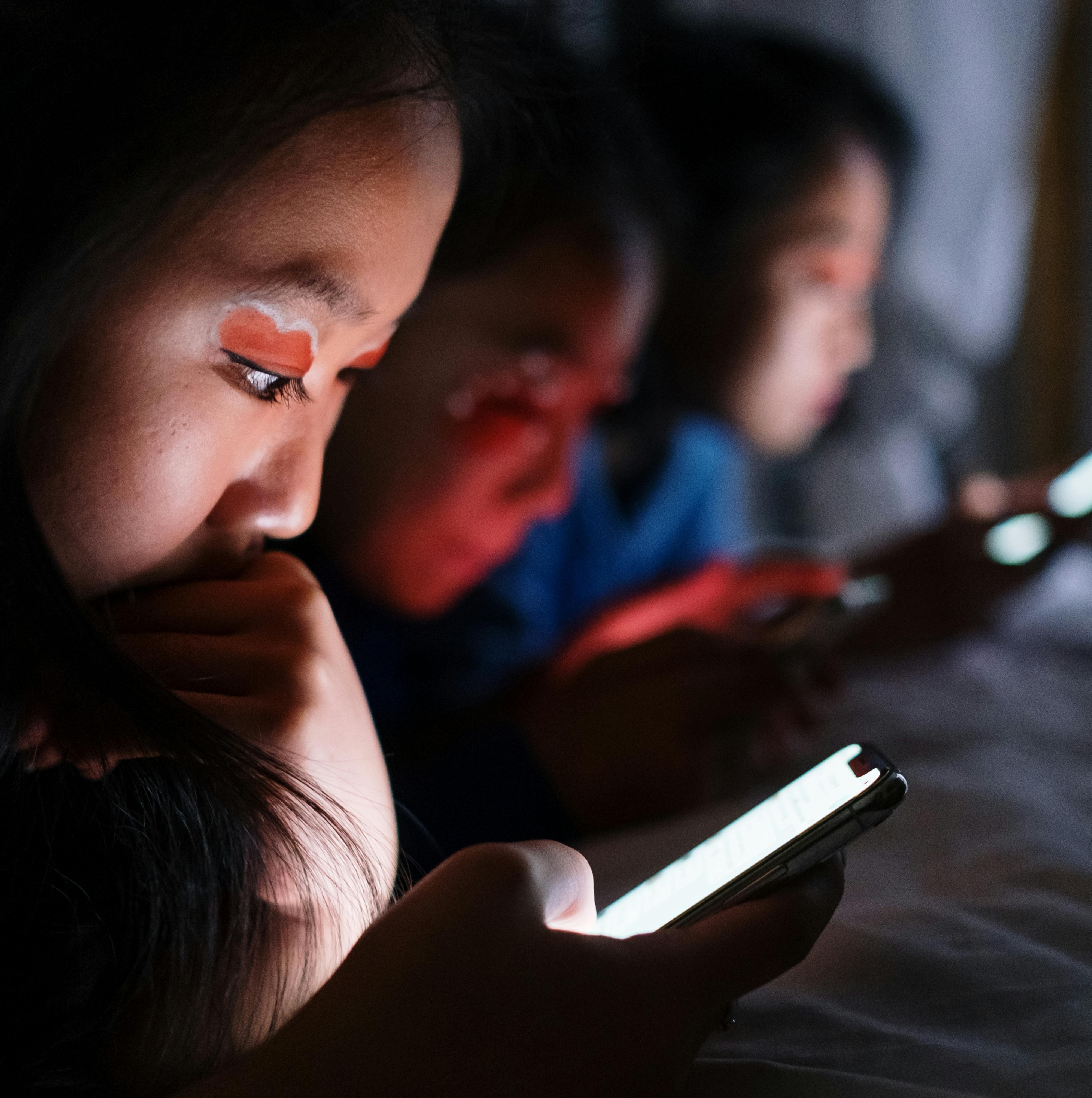 Three girls in a dark room watching smartphones