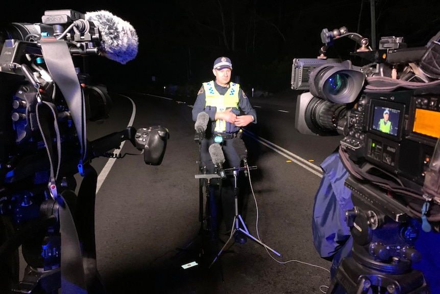 a police officer with microphones in front of microphones and two cameras. 
