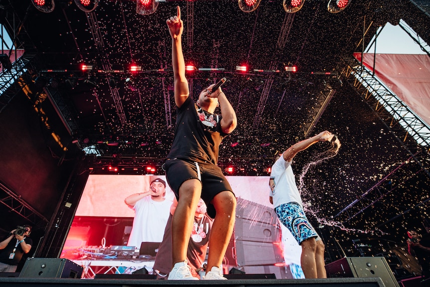 Two members of ONEFOUR performing on stage, holding mics, arms held out 