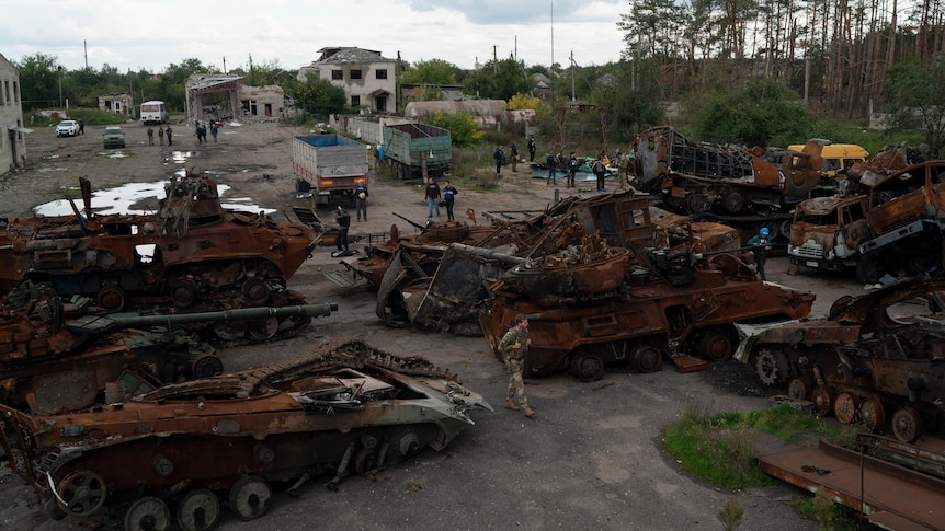 A Ukrainian serviceman and journalists walk between destroyed Russian equipment placed in the street.