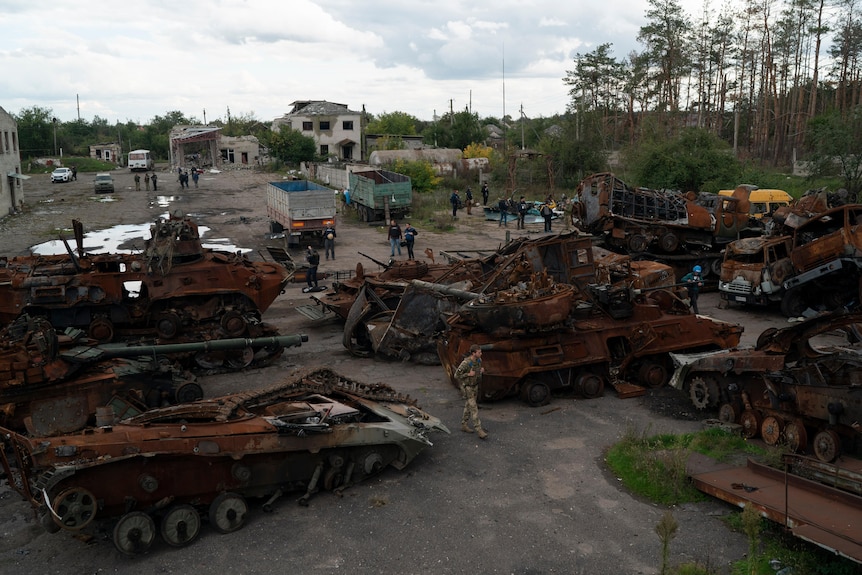 A Ukrainian serviceman and journalists walk between destroyed Russian equipment placed in the street.