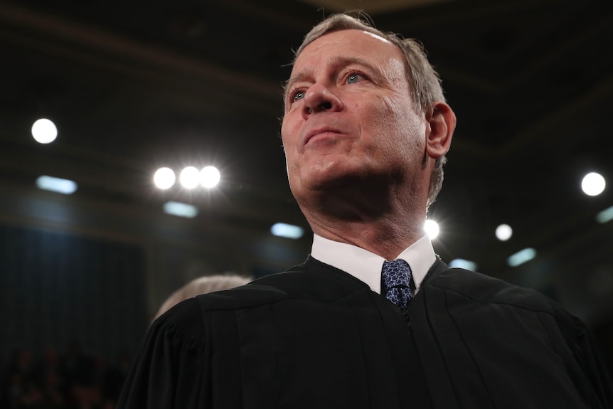 Chief Justice John Roberts, wearing his black judge's robes over a white shirt and blue tie, looks upward