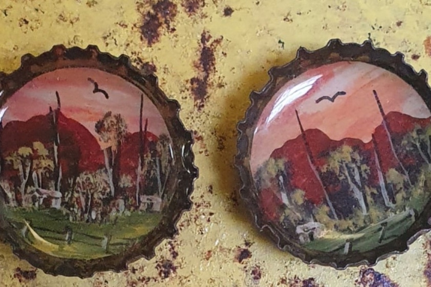 A close up of two beer bottle tops with painting inside them.