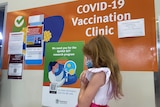A little girl in a bright dress lining up for a COVID vaccine.