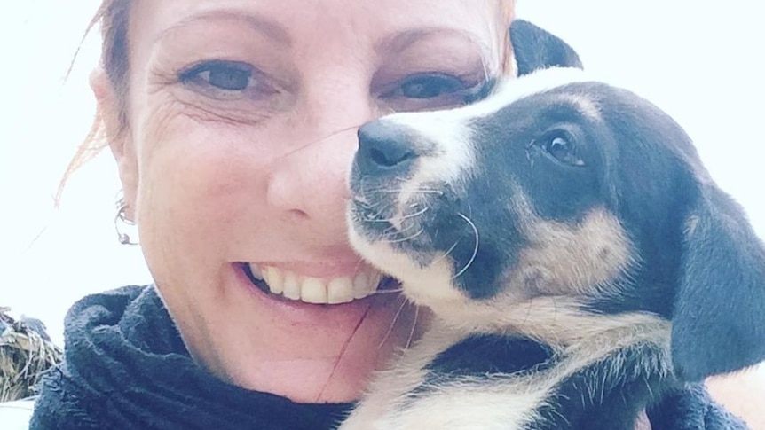 Angela Glover holds a small puppy near her face and smiles.