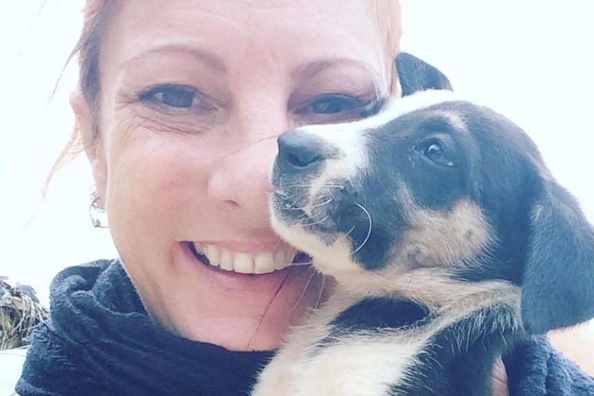 Angela Glover holds a small puppy near her face and smiles.