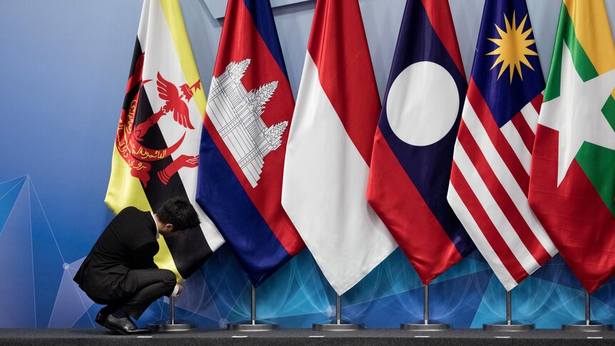 A worker adjusts Brunei's flag alongside Cambodian, Indonesian, Lao, Malaysian and Myanmar flags