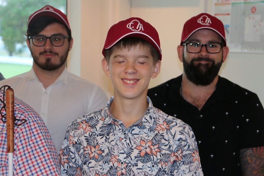 A young cricketer in a group of people wearing Queensland cricket caps