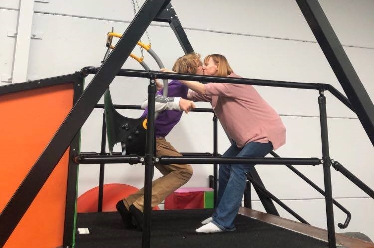 A woman kisses a child who is on accessible play equipment at an all-abilities play centre, for a story on being a carer.
