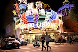 Two people walk in a street at night in front of a bright casino with colourful lights