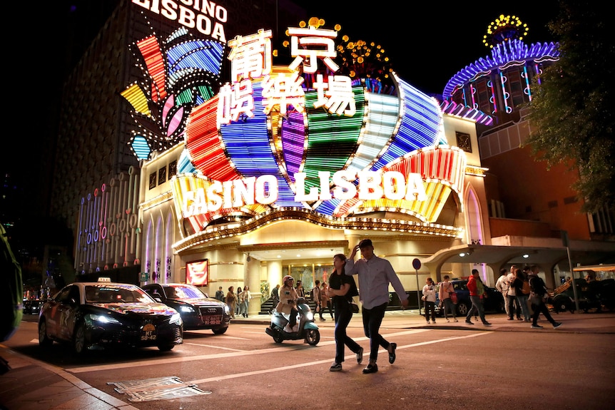Two people walk in a street at night in front of a bright casino with colourful lights