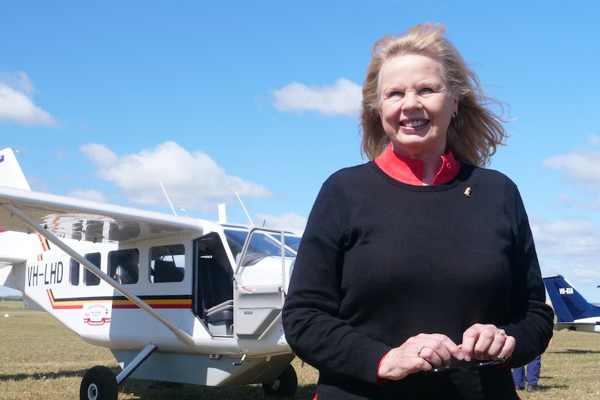 A middle-aged woman standing in front of an aeroplane looking into the distance.