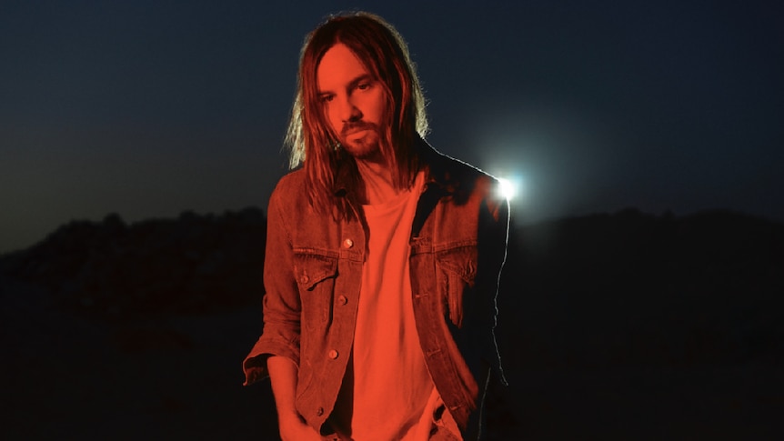 Kevin Parker photographed at night with red filter, wearing denim jacket, white shirt
