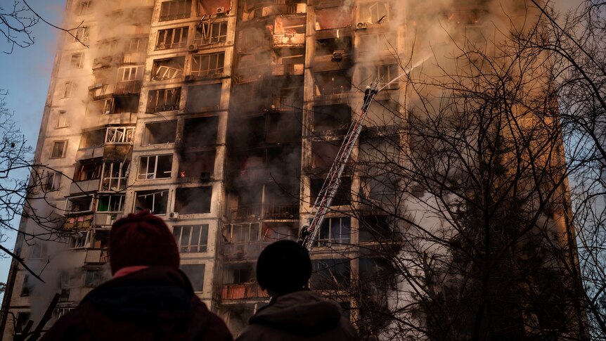 Fire crews attempt to put out a blaze as smoke rises off a scorched, shelled apartment building