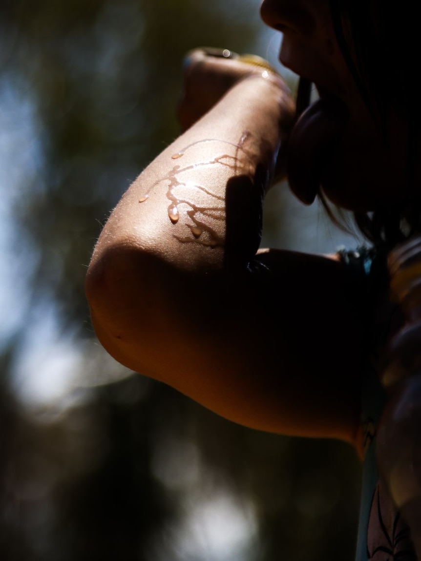 Sunlight on a child's arm, highlighting a trail of water, which they have raised up to their face. 