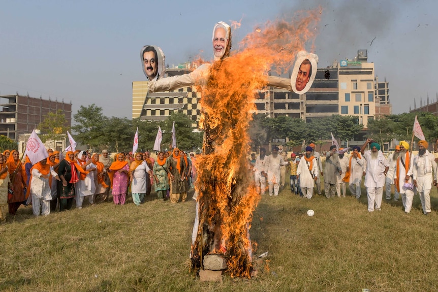 A crowd gathers around a burning effigy in a field.