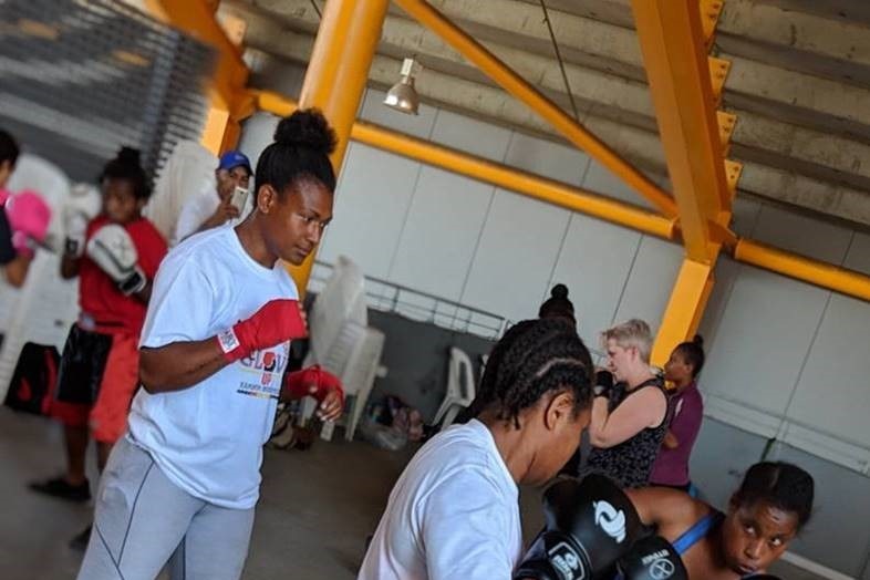 A woman wearing red gloves and work out gear watches two other women with their boxing gloves raised.