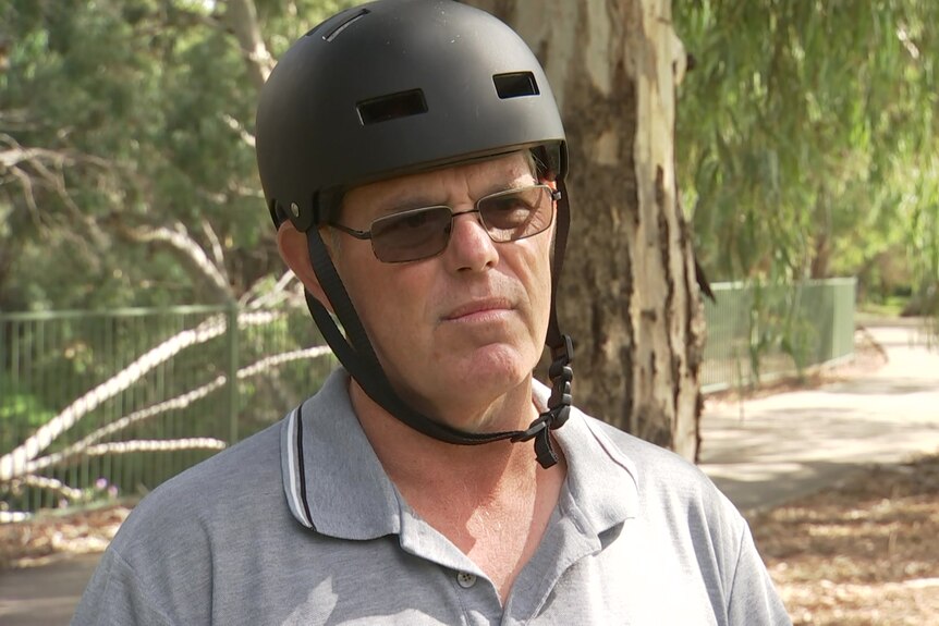A man wearing a black helmet with trees and a footpath behind him