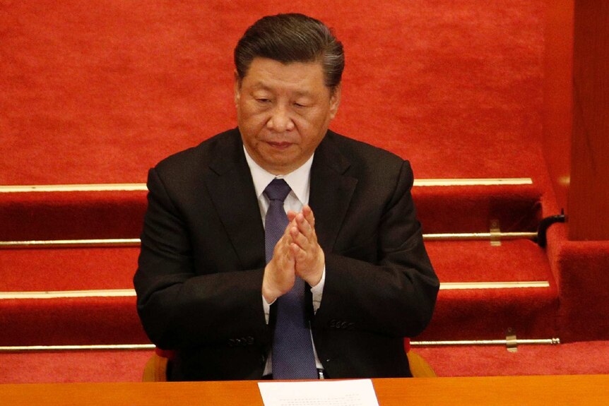 Xi Jinping claps in front of a red background