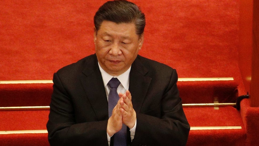 Xi Jinping claps in front of a red background