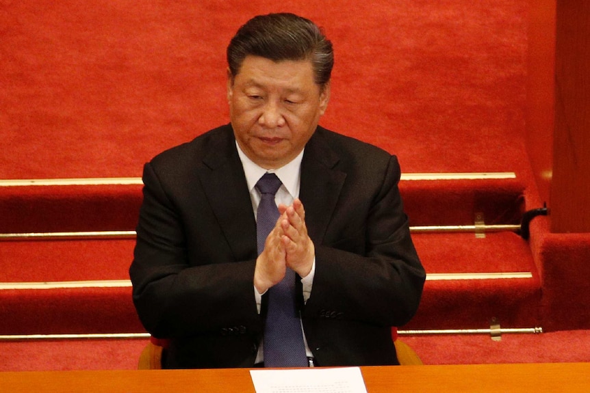 Xi Jinping claps in front of a red background