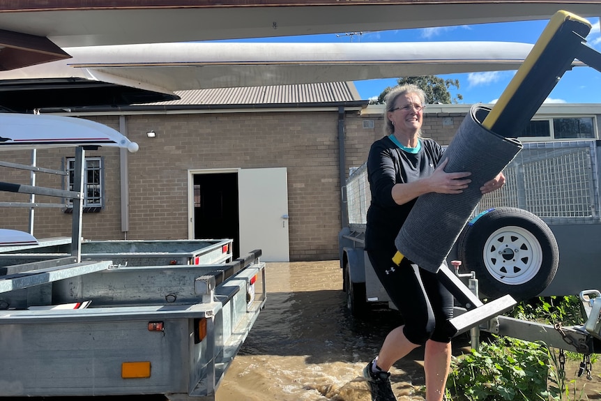 a woman moving gym equipment out of a flooded rowing club.