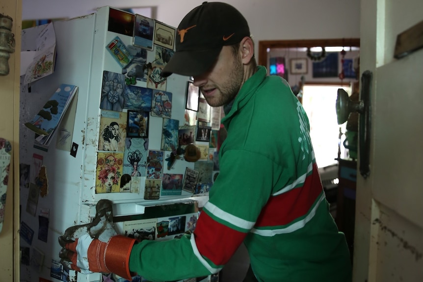 A man moves a fridge inside a house.