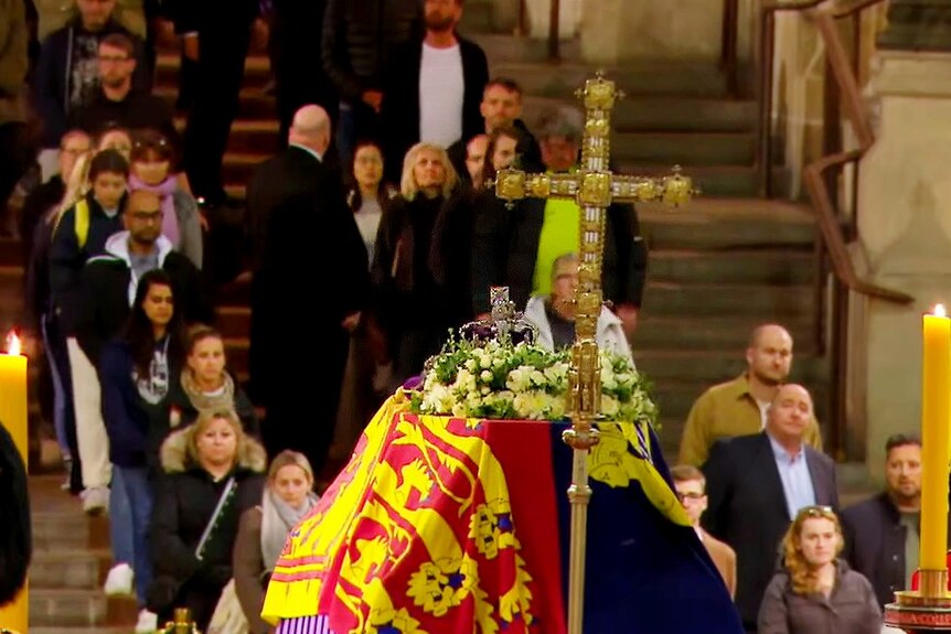 In the foreground, the queens coffin. Behind, people descend stairs to approach it