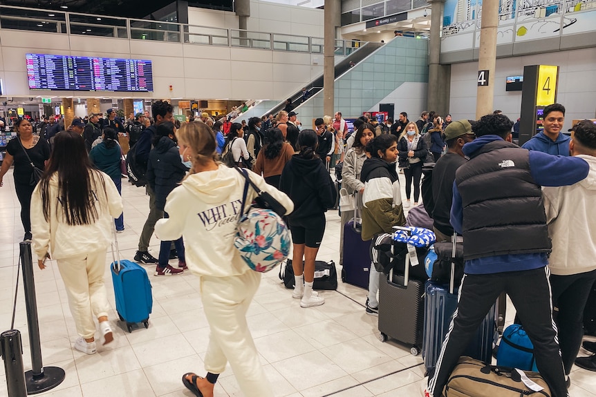 Busy Brisbane Airport with departures board in the background, people lined up to check in