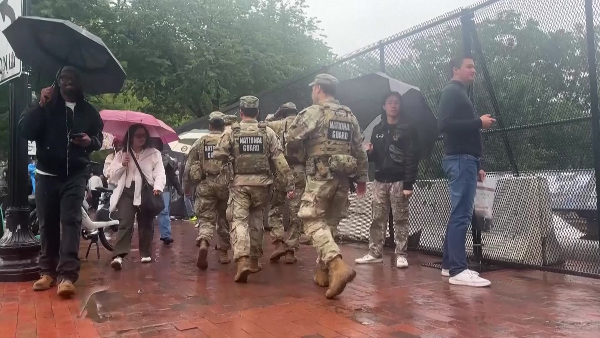 National Guard troops in army fatigues move through a crowd in front of a fence