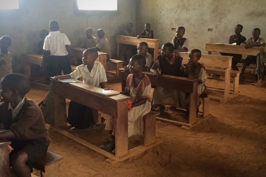 African school students sitting at wooden desks in their earth-floor classroom.