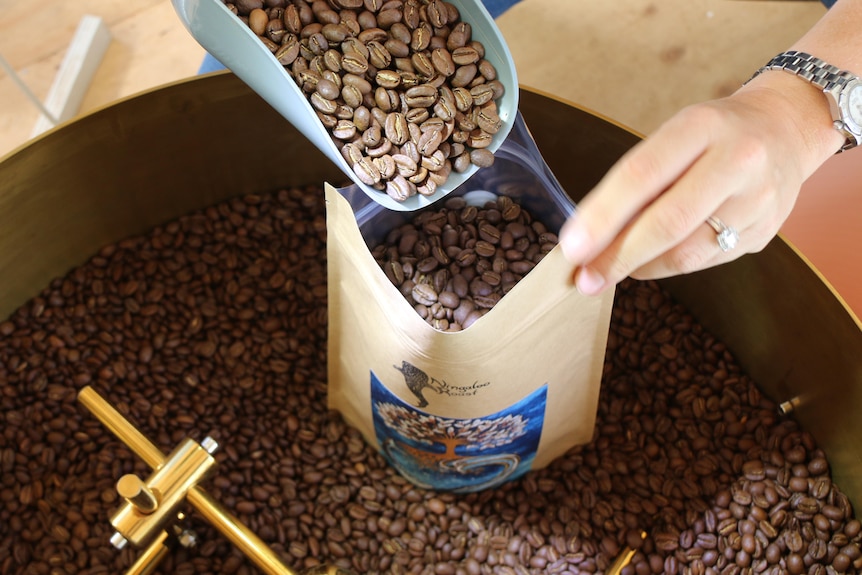 Hands scooping coffee beans into a brown paper bag for sale