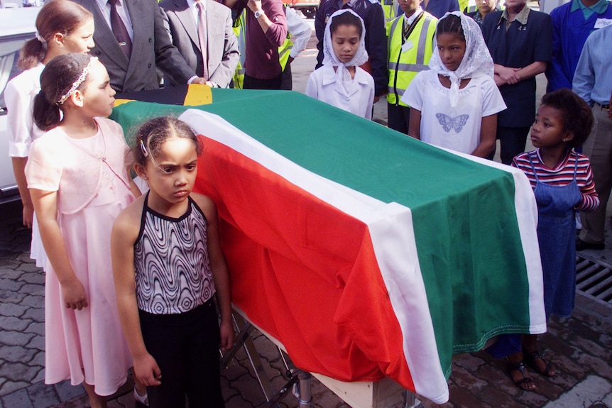 Young girls surround a coffin with red, white and green South African flag.