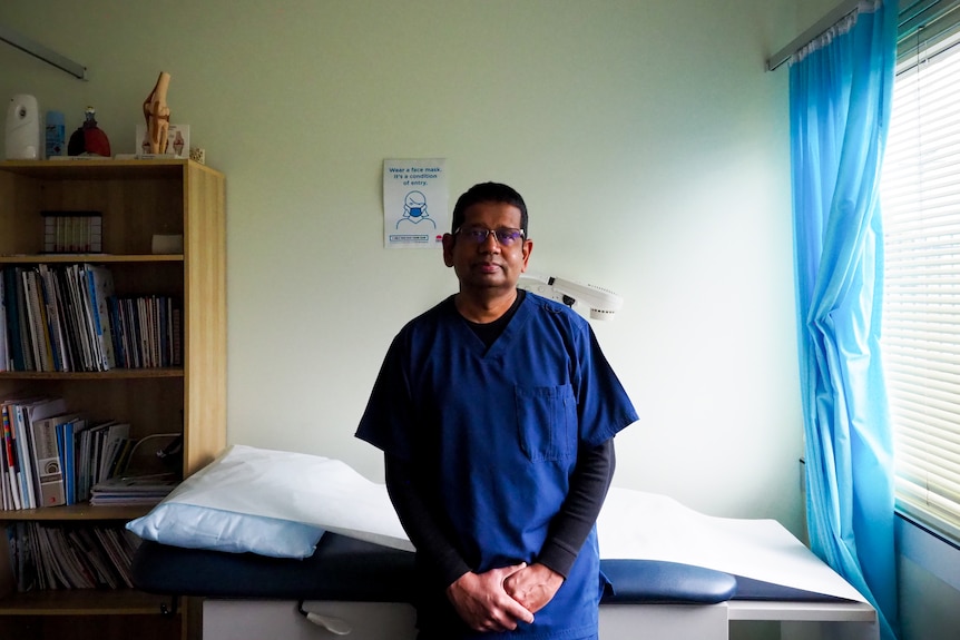 Dr Thevashangar Vasuthevan sits on the edge of a examination table in is office.