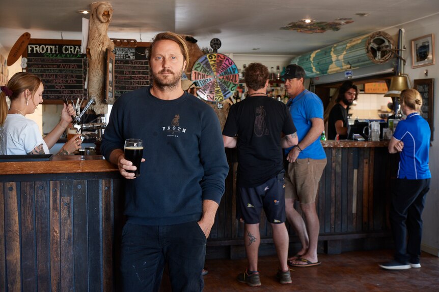 A man stands in a bar with a beer in his hand. 