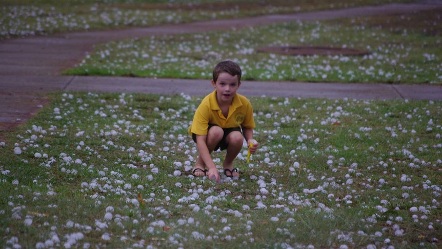 A young child bending down to pick up large hailstones.