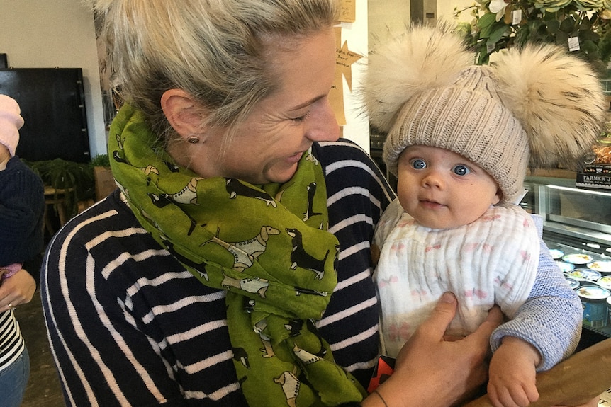 Woman holding baby in cafe, baby wearing beanie with fluffy pom poms