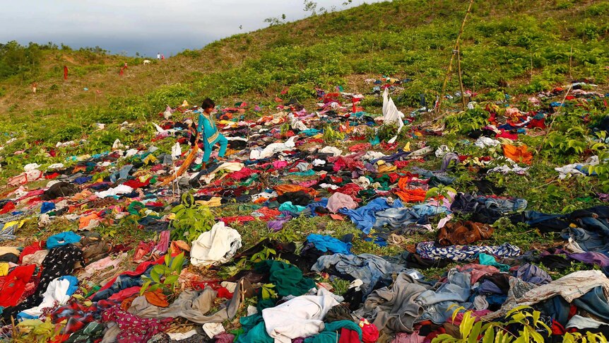A girl walks among hundreds of items of clothing spread out on a field