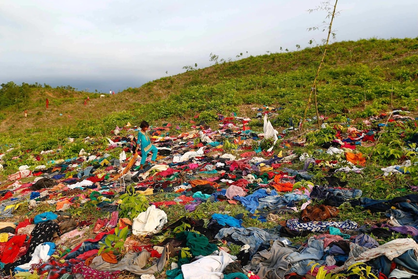 A girl walks among hundreds of items of clothing spread out on a field